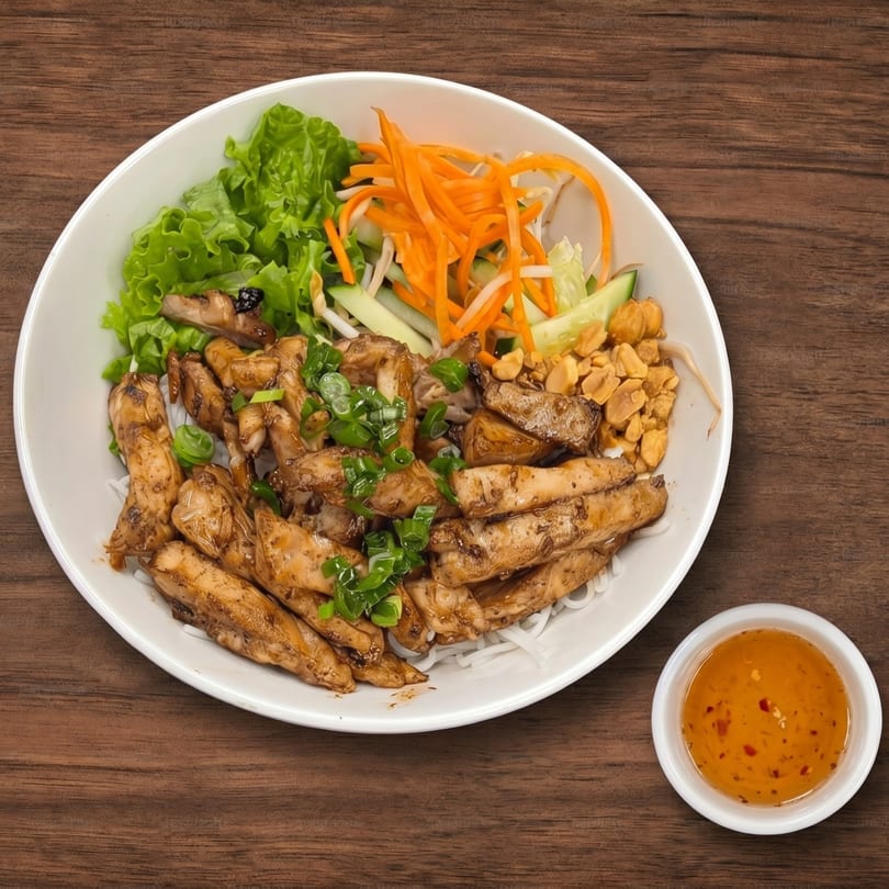 Grilled chicken, rice noodles, lettuce, carrots, cucumbers, peanuts, and scallions with a side of sauce.